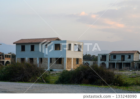 Deserted buildings stand quietly under a soft sunset sky in a forgotten development Deserted buildings stand quietly under a soft sunset sky in a forgotten development 133248090