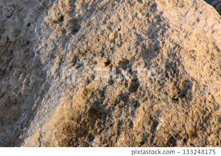 Textured stone surface captures light during golden hour near a tranquil riverbank 133248175