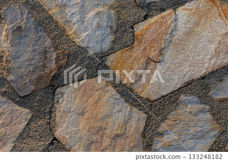 Natural stone pattern reveals earthy tones and textures in a rustic wall design during sunlight hours 133248182
