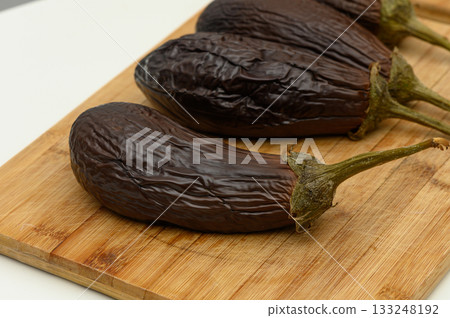 Freshly harvested eggplants on a wooden cutting board ready for culinary delights and healthy meals Freshly harvested eggplants on a wooden cutting board ready for culinary delights and healthy meals 133248192