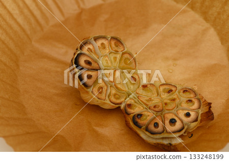 Deliciously roasted garlic bulbs showcasing their warm golden tones on parchment paper Deliciously roasted garlic bulbs showcasing their warm golden tones on parchment paper 133248199