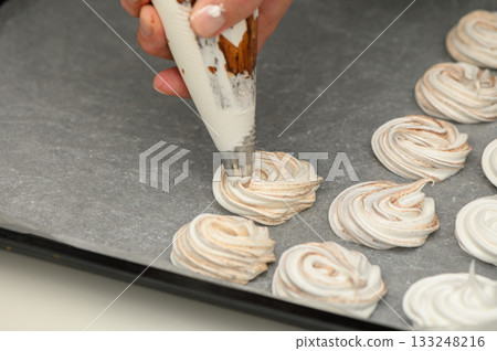 Handcrafted meringue swirls being shaped on parchment paper in a cozy kitchen setting 133248216