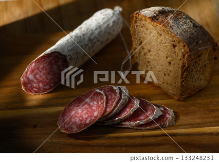 Artisan cured meat and fresh bread on a rustic wooden cutting board in soft afternoon light 133248231