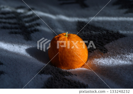 Bright orange mandarin resting on a cozy blanket in soft morning light 133248232