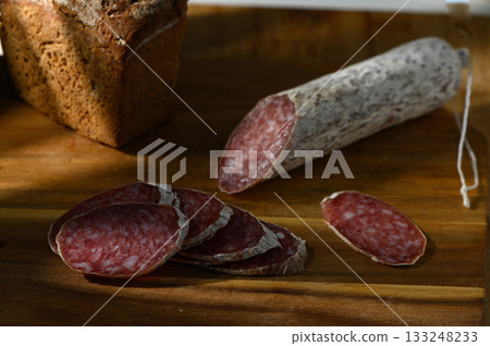 Savory slices of cured salami beside freshly baked bread on a rustic wooden board Savory slices of cured salami beside freshly baked bread on a rustic wooden board 133248233