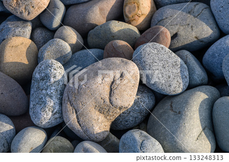 Smooth pebbles glisten in the warm sunlight along a tranquil riverbank 133248313