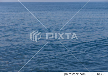 Calm blue sea stretches endlessly under a clear sky with gentle waves lapping at the shore Calm blue sea stretches endlessly under a clear sky with gentle waves lapping at the shore 133248333