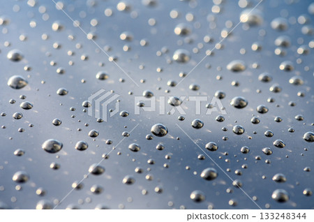 Raindrops dance on a reflective surface under a cloudy sky during a tranquil moment of nature Raindrops dance on a reflective surface under a cloudy sky during a tranquil moment of nature 133248344