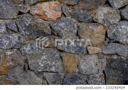 Rustic stone wall showcasing textured surfaces and varied hues in an outdoor setting 133248404