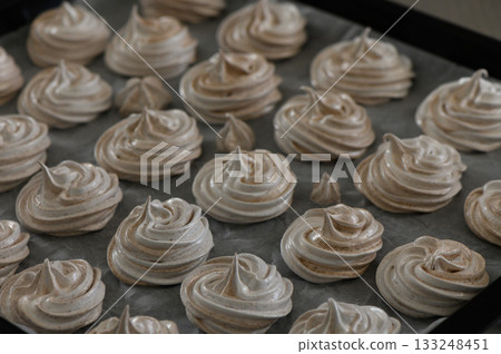 Delicate meringue cookies arranged artistically on a baking tray before baking in a cozy kitchen 133248451
