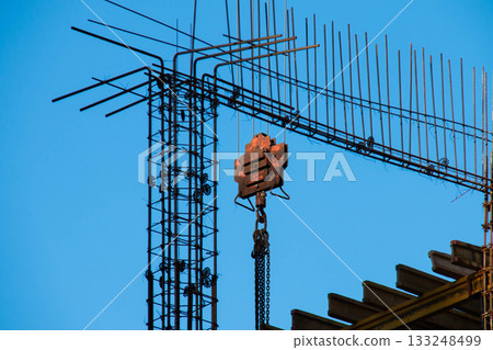 Red Rusty Hook suspension of Tower Crane surrounded by Connected Fittings on Blue Sky background in clear weather at Construction Site for Lifting and Moving Goods. Chain Covered with Rust 133248499