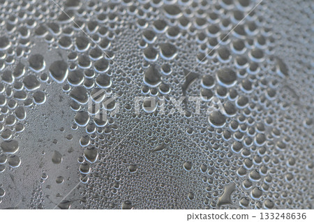 Water droplets collect on a glass surface reflecting intricate patterns under soft light 133248636