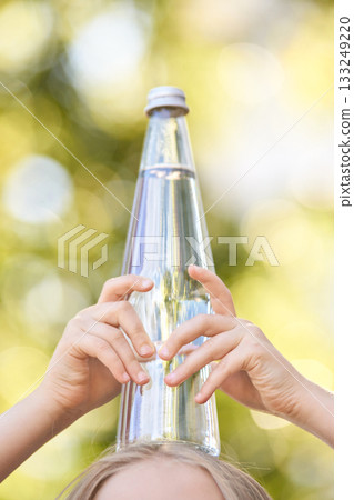 Child holding water bottle under sunlight with green bokeh background 133249220