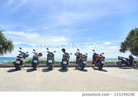Row of parked motorbikes by ocean on sunny day with blue sky and coastal Row of parked motorbikes by ocean on sunny day with blue sky and coastal 133249290