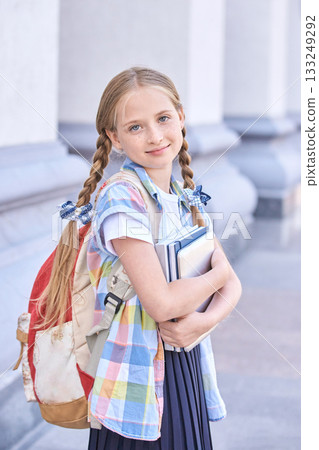 Blonde caucasian young girl with braided hair holding books and backpack Blonde caucasian young girl with braided hair holding books and backpack 133249292