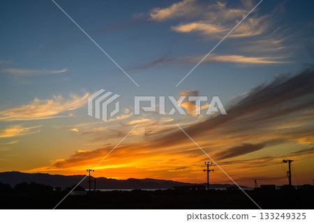 Dramatic sunset paints the sky with vibrant hues over tranquil hills and power lines in the evening light Dramatic sunset paints the sky with vibrant hues over tranquil hills and power lines in the evening light 133249325