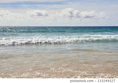 Tranquil ocean waves meeting sandy shore under clear sky on peaceful beach day 133249327