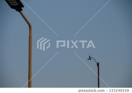 Urban landscape featuring streetlights and surveillance camera against a clear sky at dusk Urban landscape featuring streetlights and surveillance camera against a clear sky at dusk 133249339
