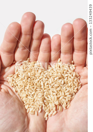 Hands holding raw brown rice grains in heart shape against white background 133249439