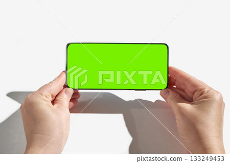 Female hands holding smartphone with green screen display on white background Female hands holding smartphone with green screen display on white background 133249453
