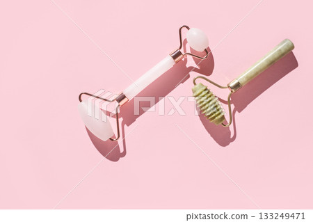 Jade and rose quartz facial rollers on pink background for skincare Jade and rose quartz facial rollers on pink background for skincare 133249471