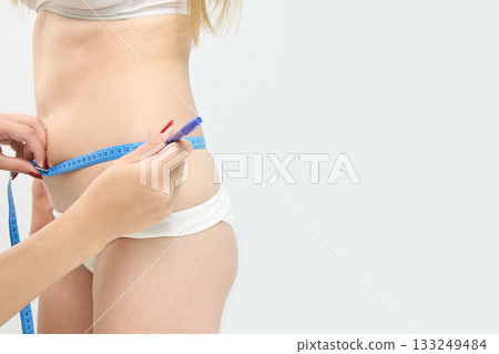Young caucasian female measuring waist with tape for fitness tracking and health 133249484