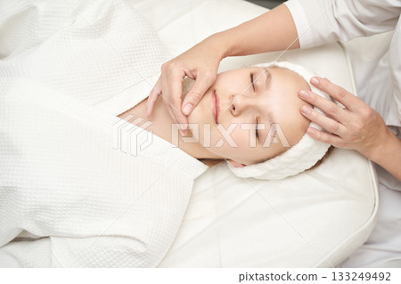 Young caucasian female relaxing during facial massage spa treatment in white 133249492