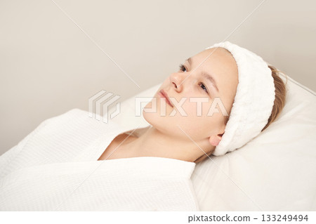Young caucasian female relaxing in spa wearing headband and white robe Young caucasian female relaxing in spa wearing headband and white robe 133249494