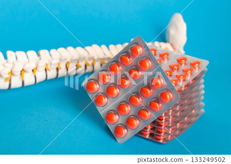 A stack of chondroprotector tablets against the background of a model of a spine on a blue background, close-up. Copy space for text 133249502