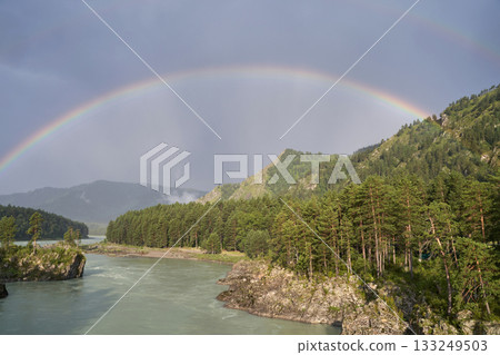 Majestic double rainbow over forested mountains and river under cloudy sky 133249503