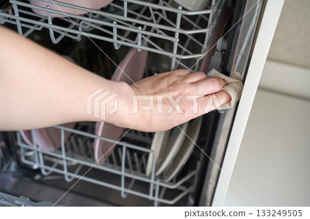 Caucasian female hand cleaning dishwasher interior with cloth ensuring hygiene 133249505