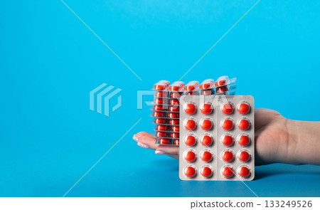 Stack of red pills in hand on blue background for edema. Diuretic pills for urethritis. Copy space for text, metabolism 133249526