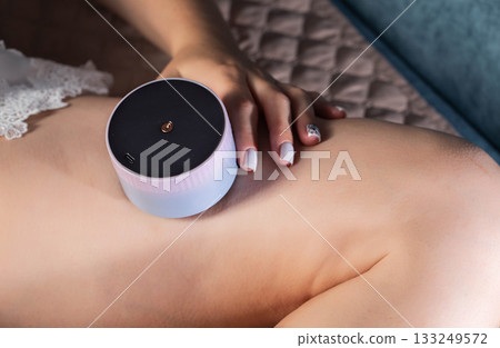 Girl gives herself a massage with a portable vacuum massager on her body. Anti-cellulite and relaxing massage, close-up 133249572