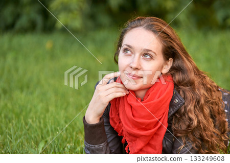 Caucasian young adult female relaxing on grass, wearing red scarf, thoughtful Caucasian young adult female relaxing on grass, wearing red scarf, thoughtful 133249608