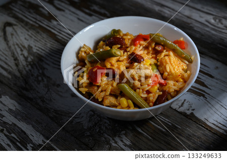 Savory rice dish brimming with colorful vegetables and tender chicken on a rustic wooden table Savory rice dish brimming with colorful vegetables and tender chicken on a rustic wooden table 133249633
