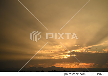 Golden rays break through clouds at sunset over the horizon with a tranquil ambiance in the early evening hours 133249635