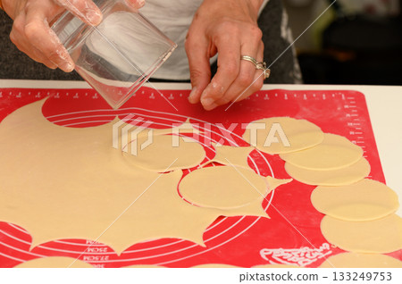 Delicate hands shape fresh pasta circles on a vibrant red surface during a culinary journey 133249753