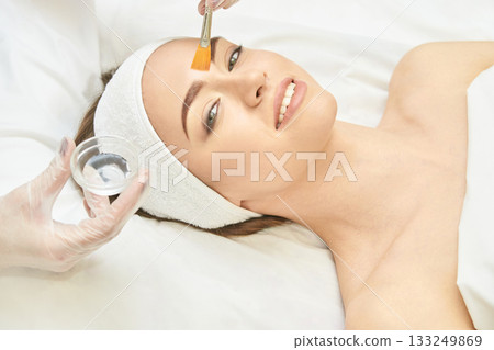 Young caucasian female receiving facial treatment with brush application in spa Young caucasian female receiving facial treatment with brush application in spa 133249869