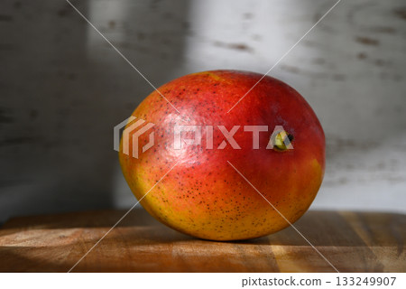 Vibrant mango resting on a wooden surface with soft light casting gentle shadows Vibrant mango resting on a wooden surface with soft light casting gentle shadows 133249907