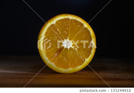 Freshly cut orange reveals juicy segments on dark wooden surface in a cozy kitchen Freshly cut orange reveals juicy segments on dark wooden surface in a cozy kitchen 133249918