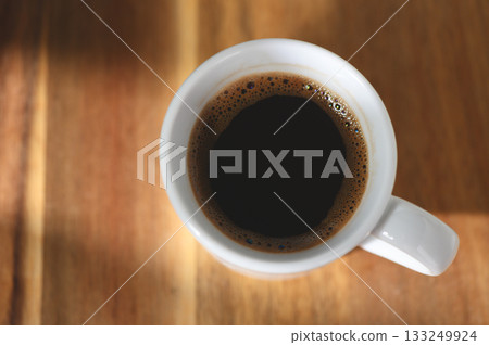 Dark coffee in a white mug resting on a wooden table with soft lighting in the morning 133249924