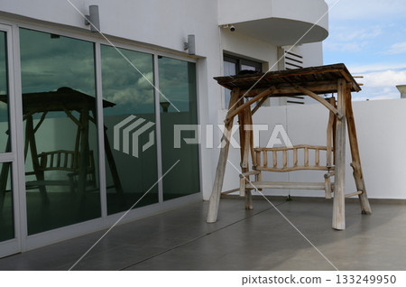 Swinging gently in the breeze, a wooden bench invites relaxation against a backdrop of modern archit 133249950