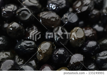 Rich and glossy black olives glisten in natural light with a hint of gourmet allure for culinary delights 133249991