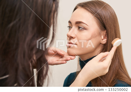 Young caucasian female receiving makeup contouring tutorial from artist Young caucasian female receiving makeup contouring tutorial from artist 133250002
