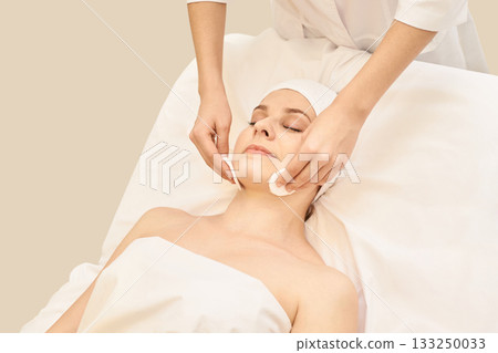 Relaxed caucasian adult female receiving professional facial spa treatment 133250033