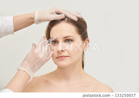 Caucasian female receiving cosmetic injection treatment by gloved hands Caucasian female receiving cosmetic injection treatment by gloved hands 133250057