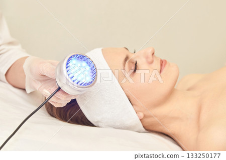 Caucasian adult woman receiving blue light therapy facial treatment in spa 133250177