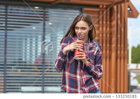 Young caucasian female enjoying a soda outdoors in casual plaid shirt Young caucasian female enjoying a soda outdoors in casual plaid shirt 133250193