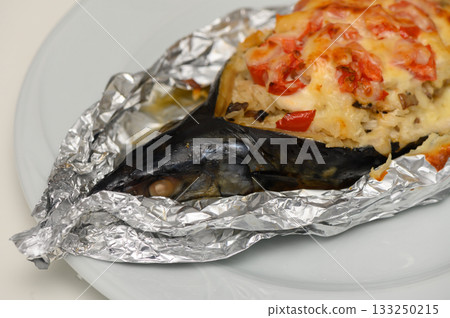 Culinary delight featuring baked fish and savory stuffing with colorful vegetables under a silver foil wrap 133250215