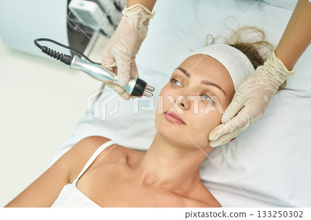 Female receiving facial treatment with modern beauty device in spa setting 133250302